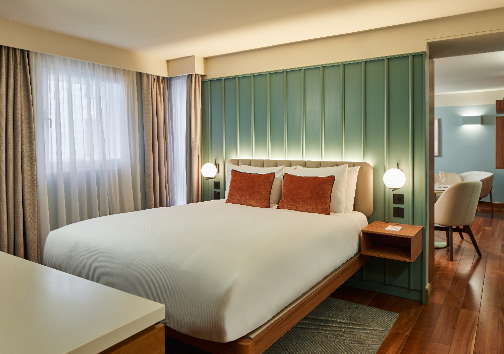 Spacious bedroom area at master Farringdon London serviced apartments, showing a cozy bed, wooden wardrobe, and view towards the open plan living area.