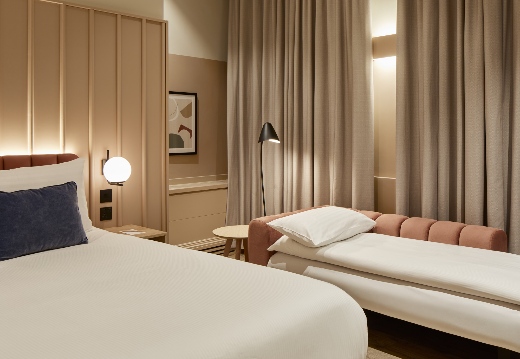 Studio at master Cannon London with a large bed and sofa bed set up for sleeping, next to elegant curtains and soft lighting.