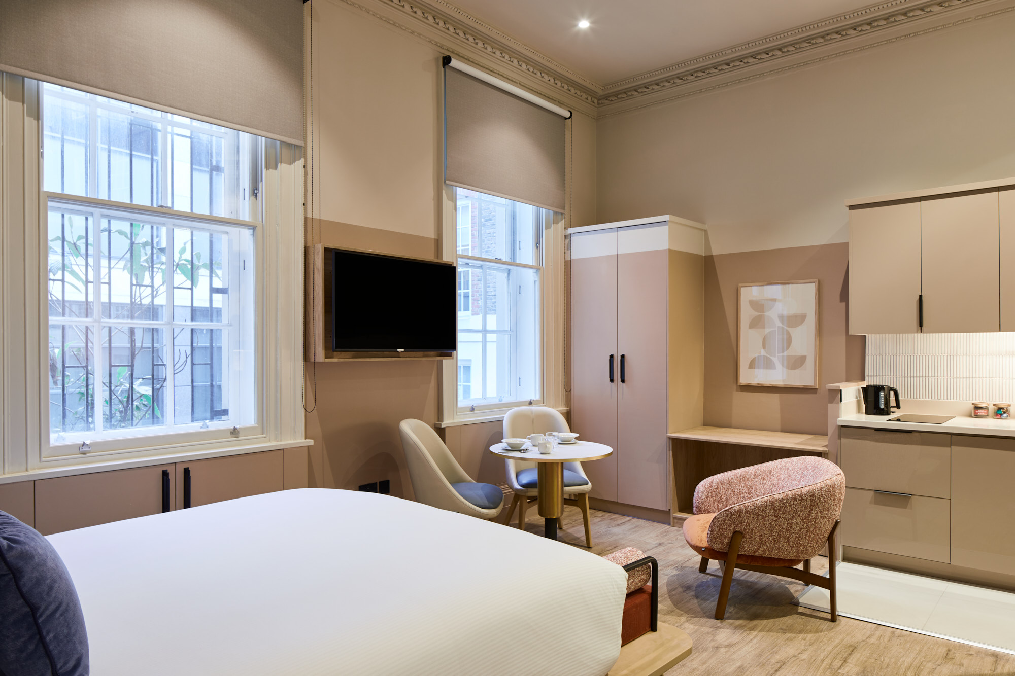 Spacious studio at master Cannon London with a modern kitchen, small dining table, comfortable bed, and elegant neutral palette accented by soft furnishings.