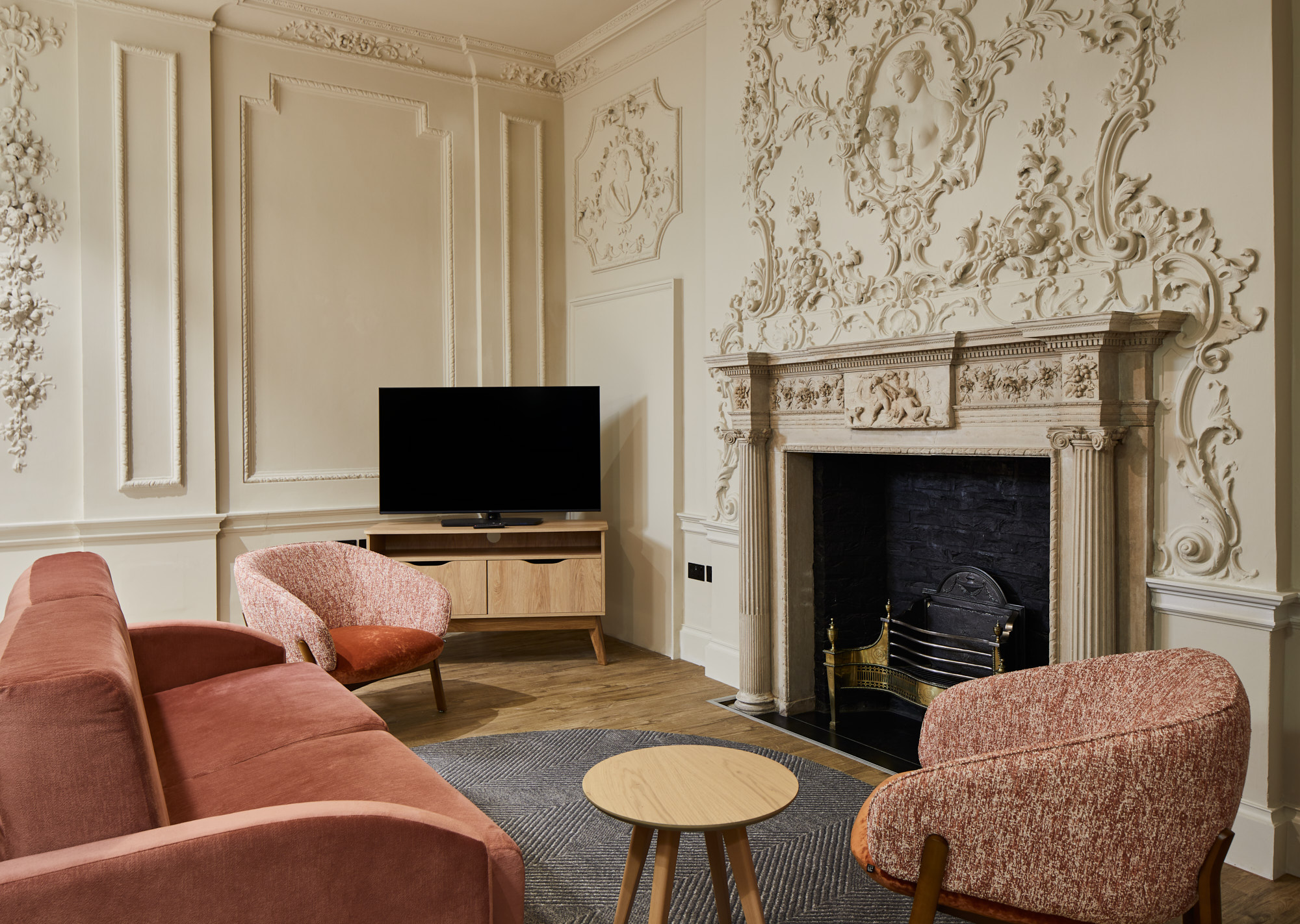 Lounge view featuring detailed plasterwork on walls, pink sofa, TV, and decorative fireplace.
