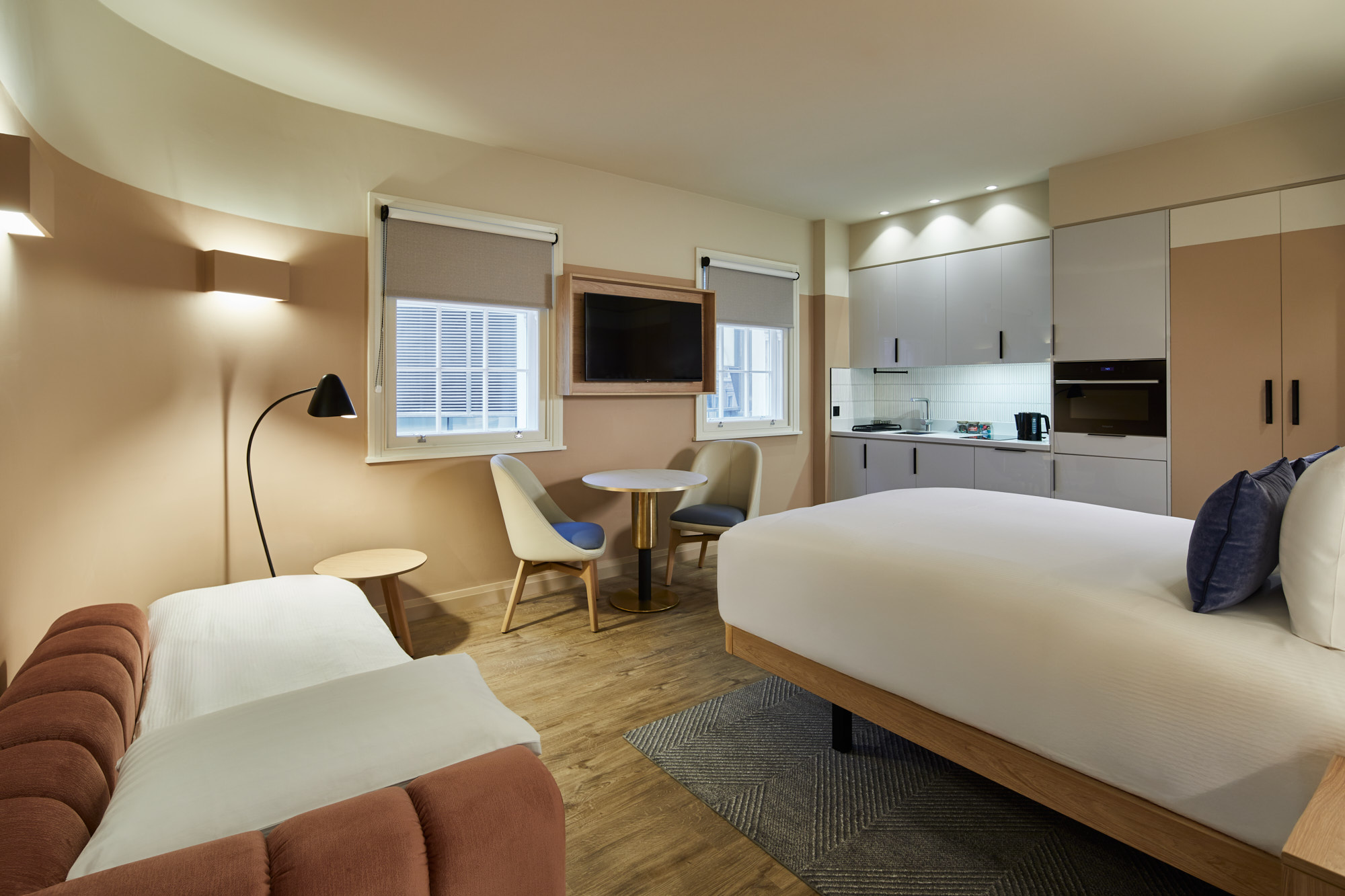 Bright studio at master Cannon London with sofa bed prepared for sleeping, modern kitchenette, and two large windows with natural light.