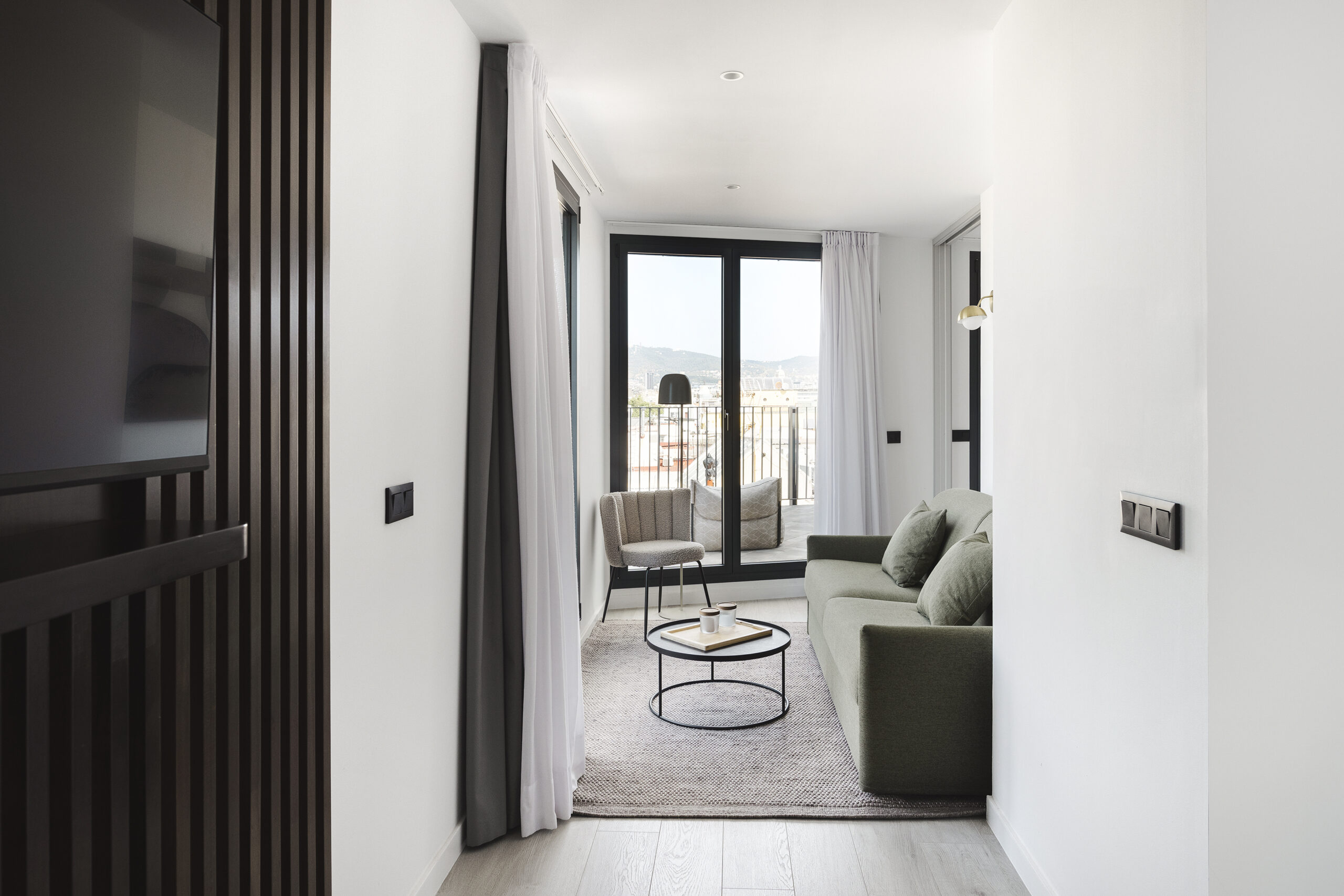 Bright living room at master La Rambla Barcelona with green sofa, round coffee table, and access to a spacious terrace with city views.