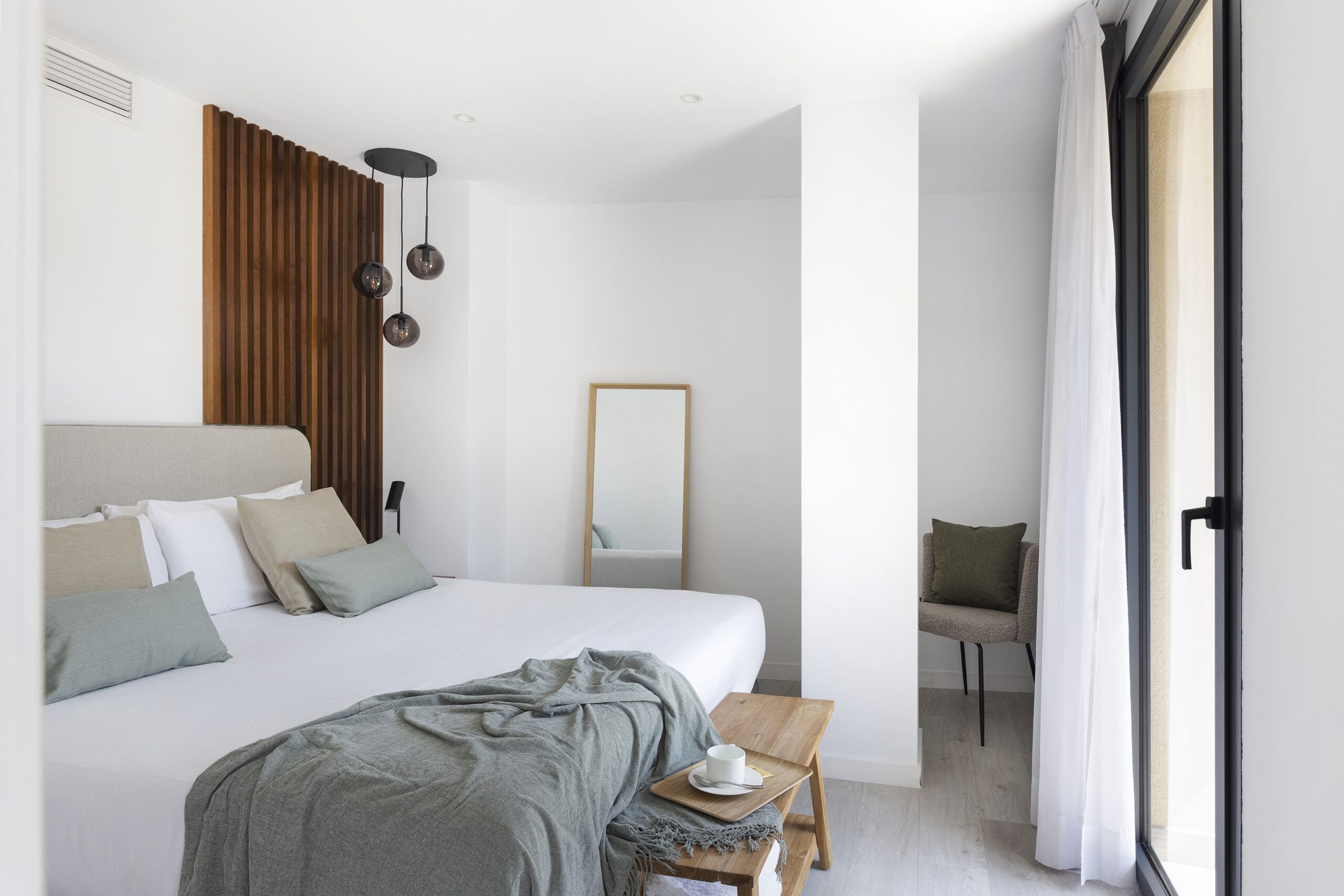 Bright bedroom at master La Rambla Barcelona with double bed, wood-panel accent wall, pendant lights, and full-length mirror.