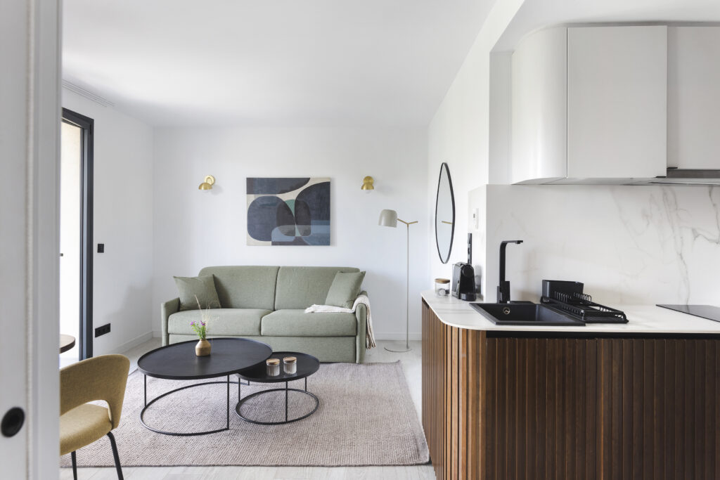Contemporary living space at master La Rambla Barcelona with sofa, round coffee tables, and fully equipped kitchen.