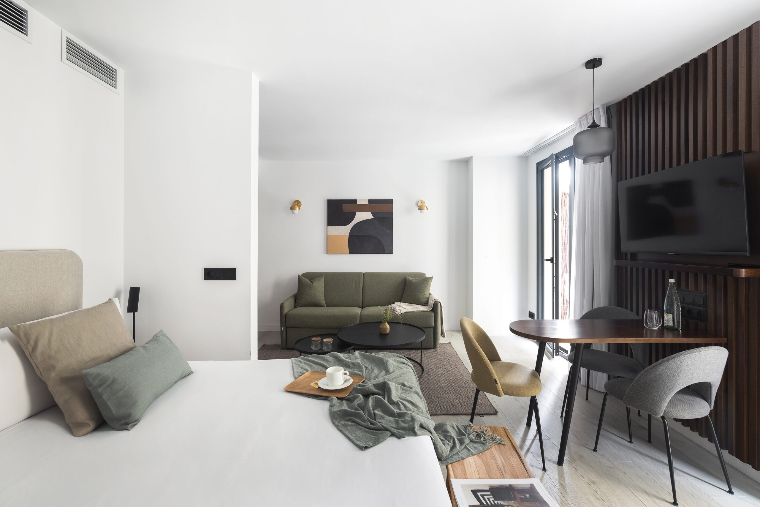 Modern studio apartment at master La Rambla Barcelona featuring a bed, sofa, dining table, and flat-screen TV with contemporary décor.