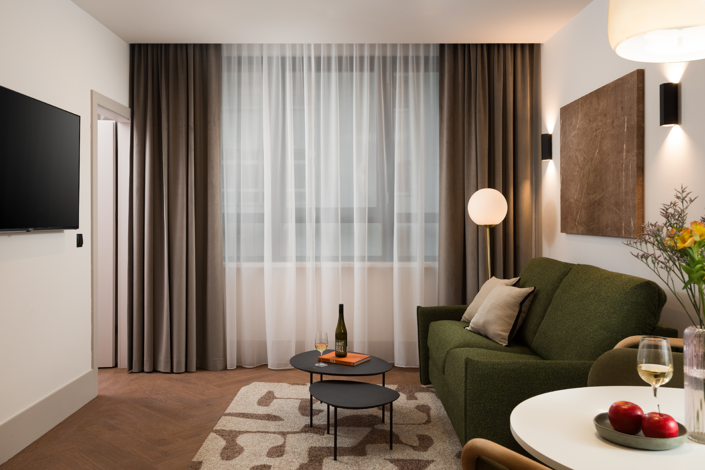 Living area of the Family Apartment at master Wola Warsaw with green sofa, coffee table, soft lighting, and large window with curtains.