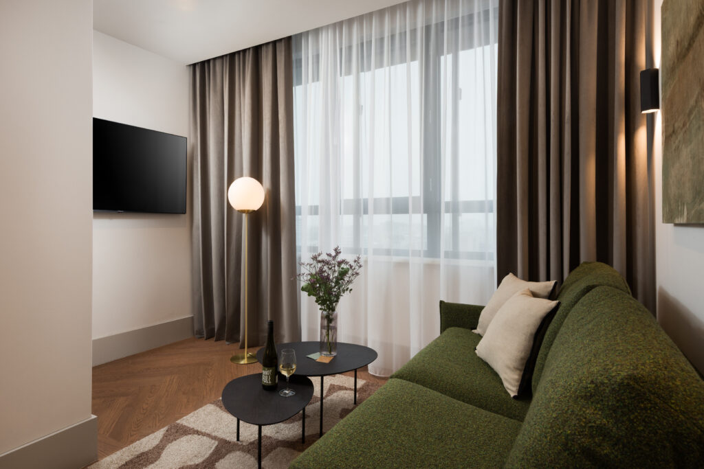 Living room corner at master Wola Serviced Apartments with green sofa, coffee table, floor lamp, and large window