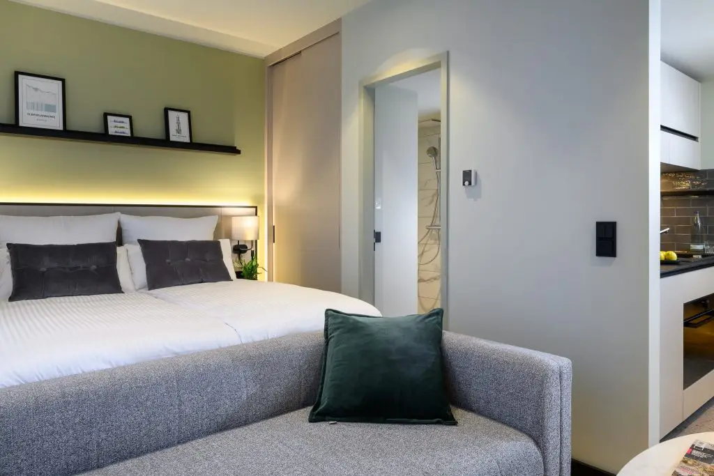 A compact studio with a gray sofa, small table, and window with sheer curtains