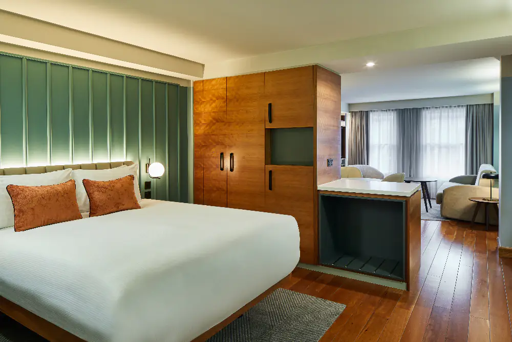 Bright bedroom at master Farringdon London serviced apartments, with a large comfortable bed, warm tones, and floor-to-ceiling curtains.