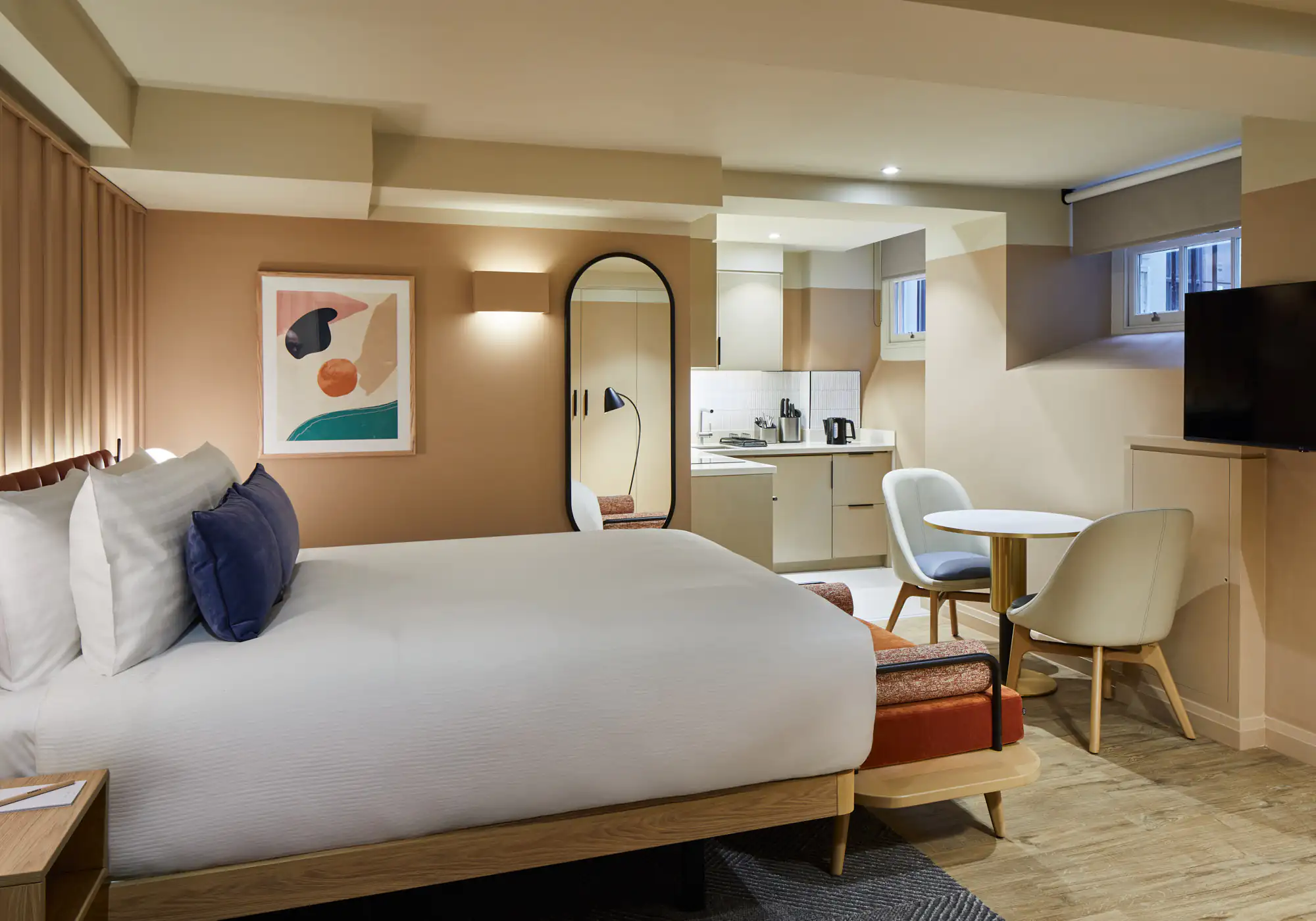 Lower ground studio at master Cannon London with a large bed, soft neutral tones, compact kitchen, dining table, and abstract wall art.