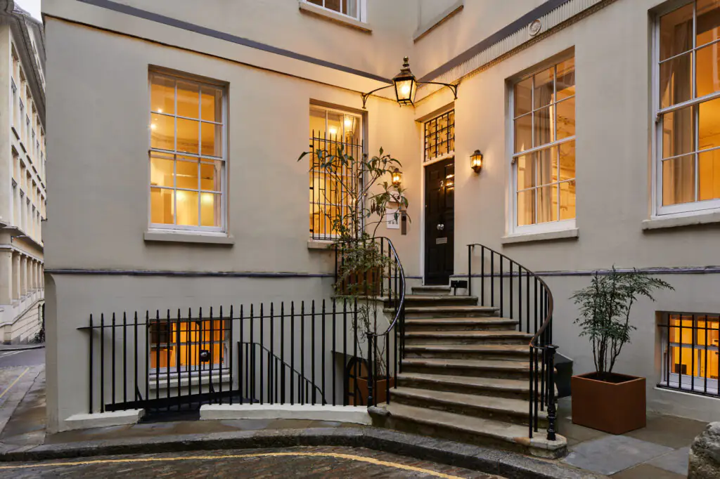 Elegant exterior entrance of master Cannon London apartments featuring warmly lit windows, classic architecture, and a charming curved staircase.