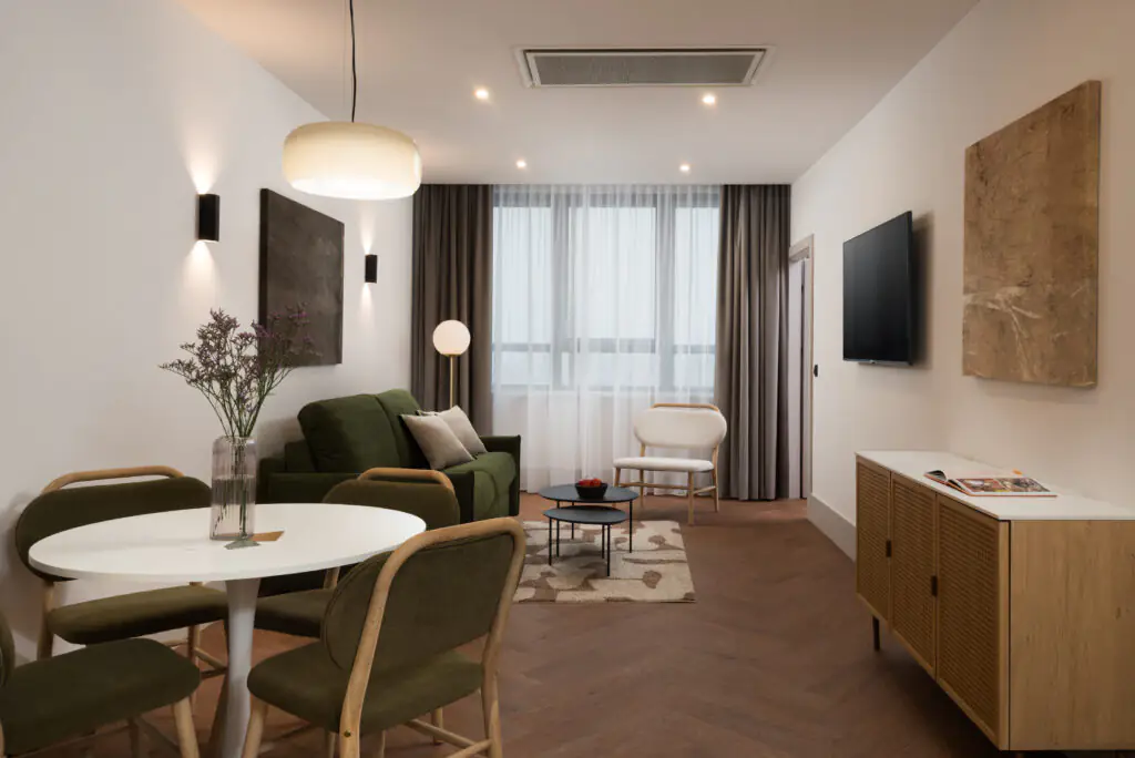 Modern living and dining area at master Wola Serviced Apartments with green sofa, round dining table, and soft natural light